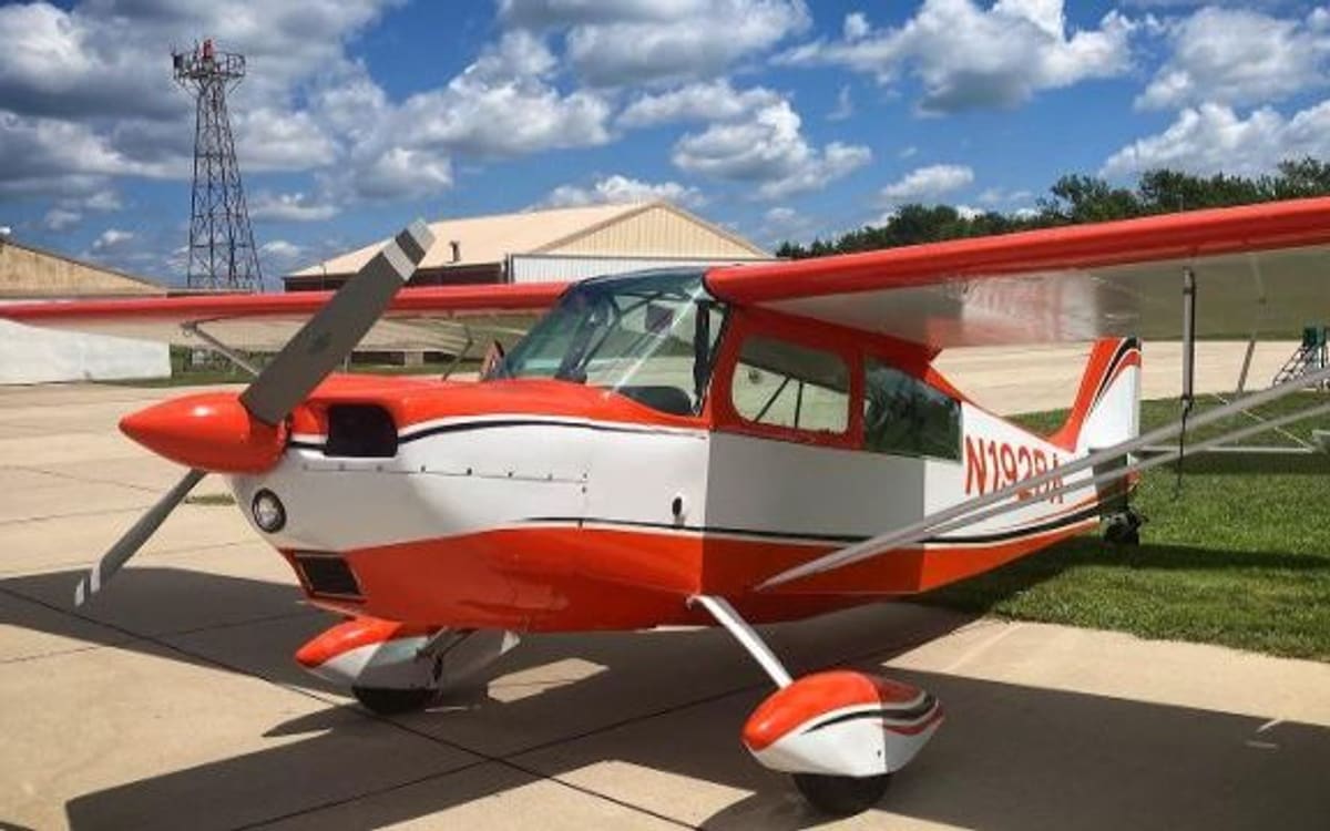 An orange-and-white Citabria taildragger on a sunlit ramp, tail wheel down and propeller stopped.